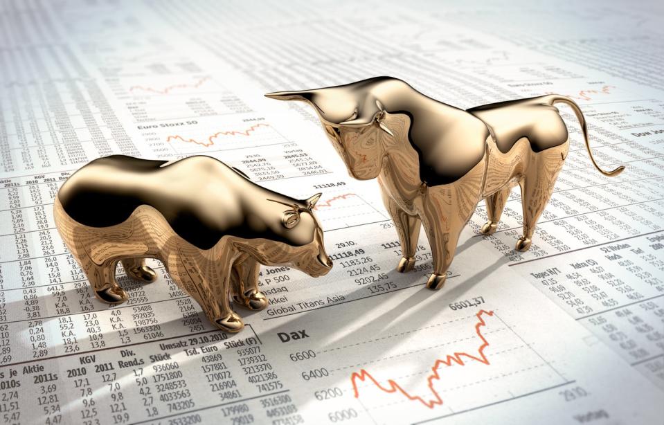 Golden bull and bear figurines standing on a newspaper's financial page.